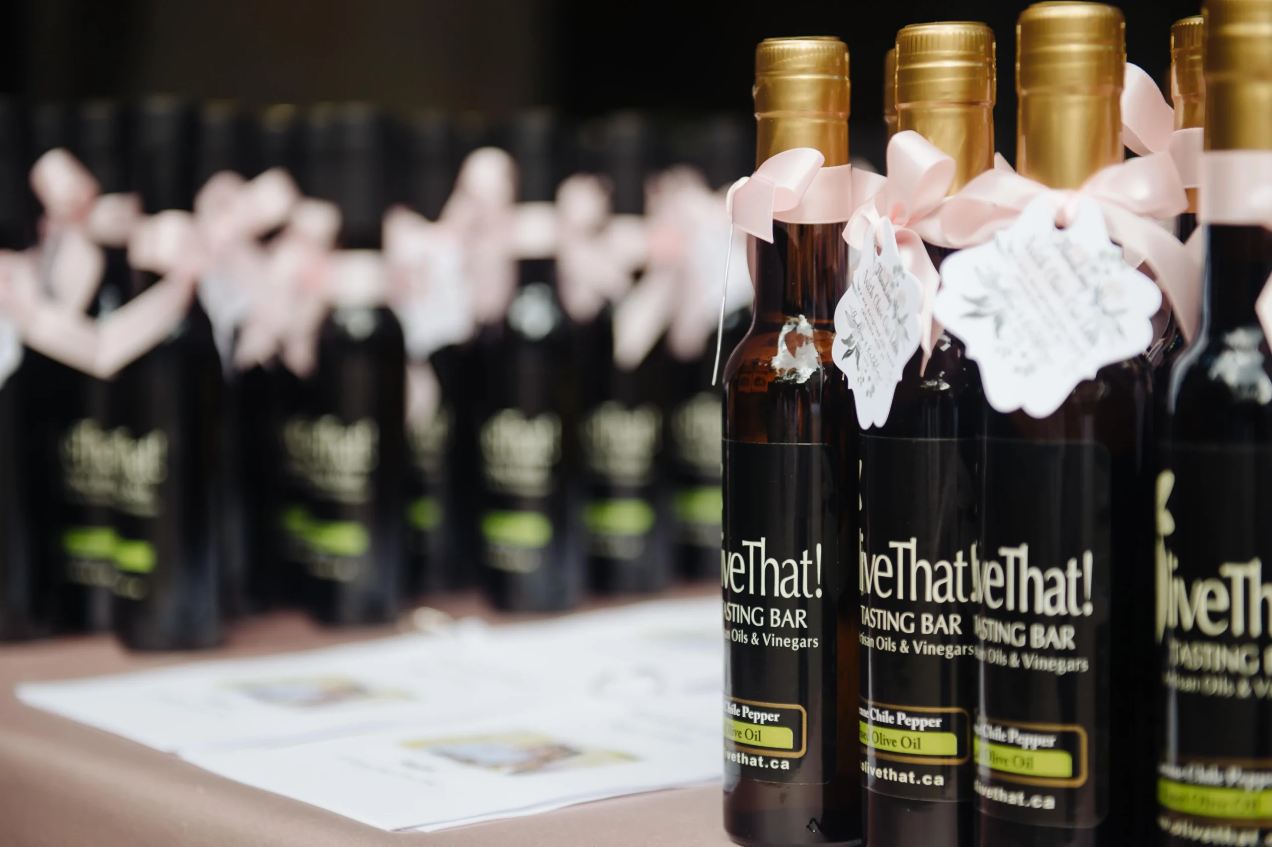 Olive That! wedding favour bottles with pink ribbons lined up for a wedding reception