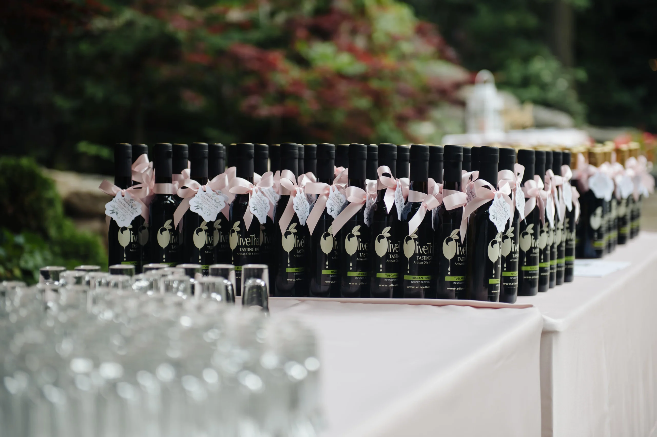Olive That! 200ml favour bottles with pink ribbons lined up on an outdoor wedding display table