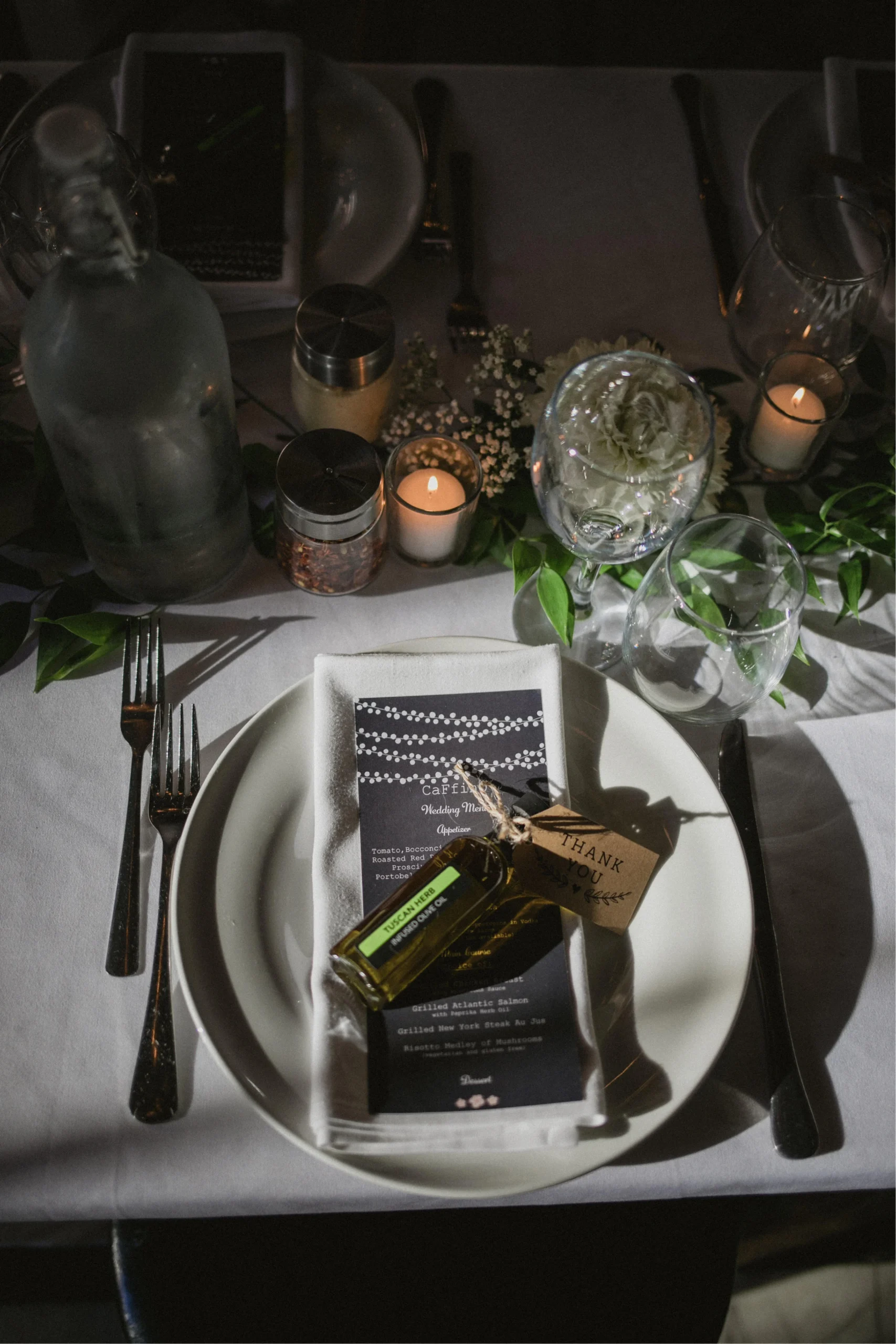 Dark moody wedding table with greenery runner, candles, and olive oil favour bottles